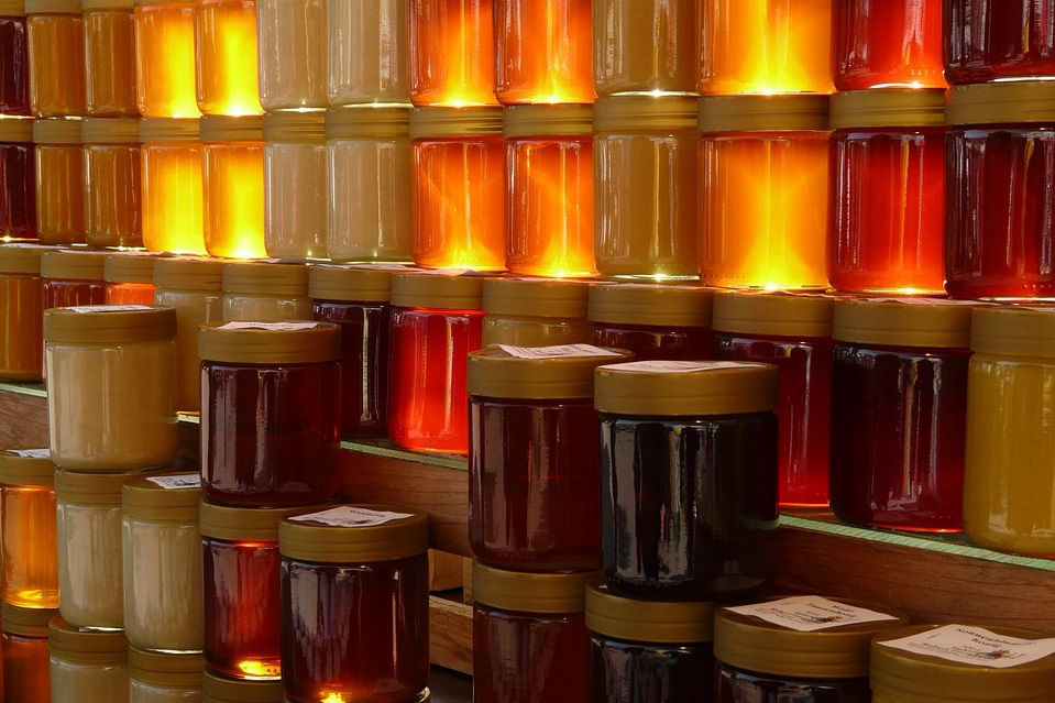 Honey varieties in transparent glass jars stacked one on top of the other showing off their colors under natural light